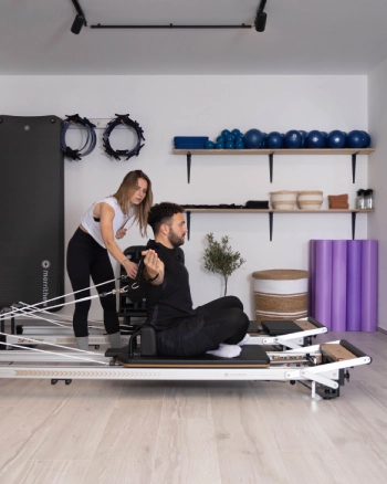 Pilates coach adjusting a male student for correct posture and optimal strengthening.