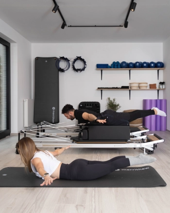 Pilates exercise: man on reformer and woman on mat, combining muscle strengthening and flexibility.